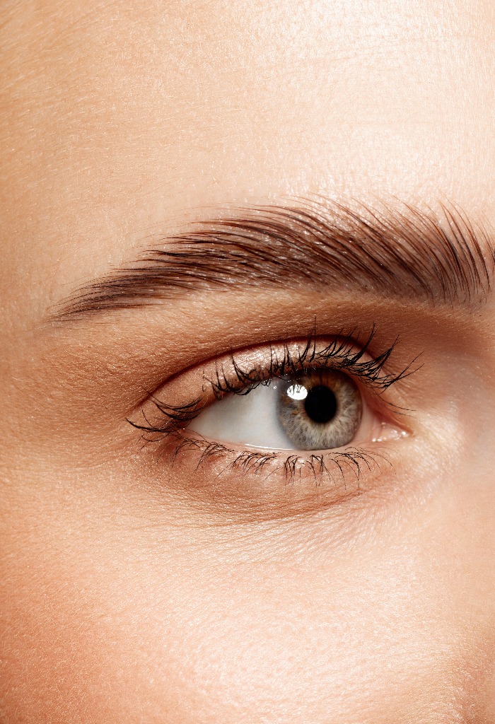 Close-up of beautiful clear female face with attractive gray eyes, perfect eyebrows and natural lashes. Eyebrow and lash lamination. Concept of makeup, cosmetics, natural beauty, skin care products