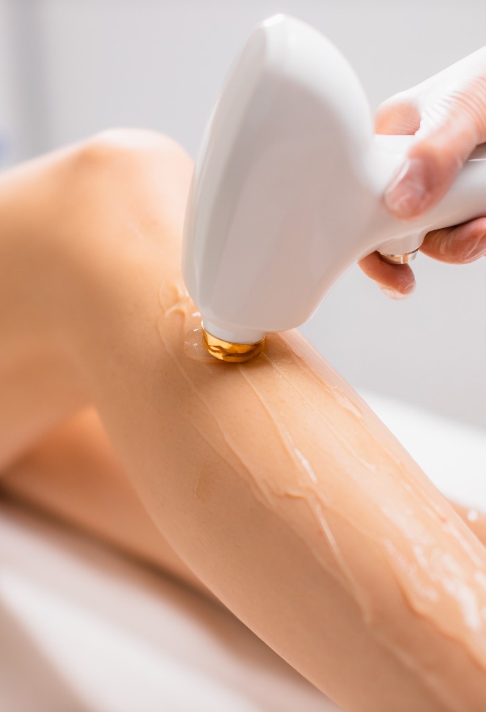 close-up woman's perfect legs while getting hair removal procedure in salon. professional beautician or cosmetologist use special ointment and apparatus. soft and smooth hairless skin on legs