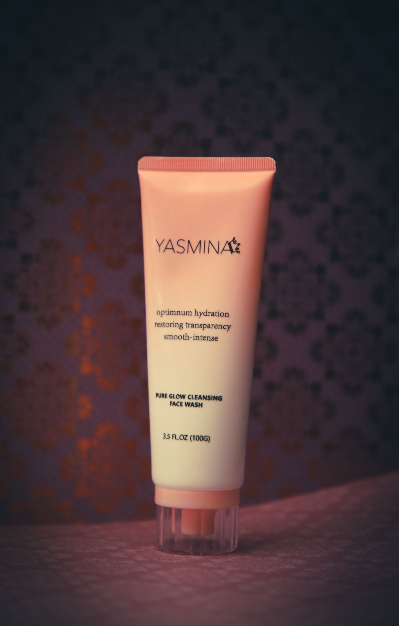 Rosa Tube mit Gesichtspflege, Text: Yasmina, auf einem dekadenten Hintergrund.