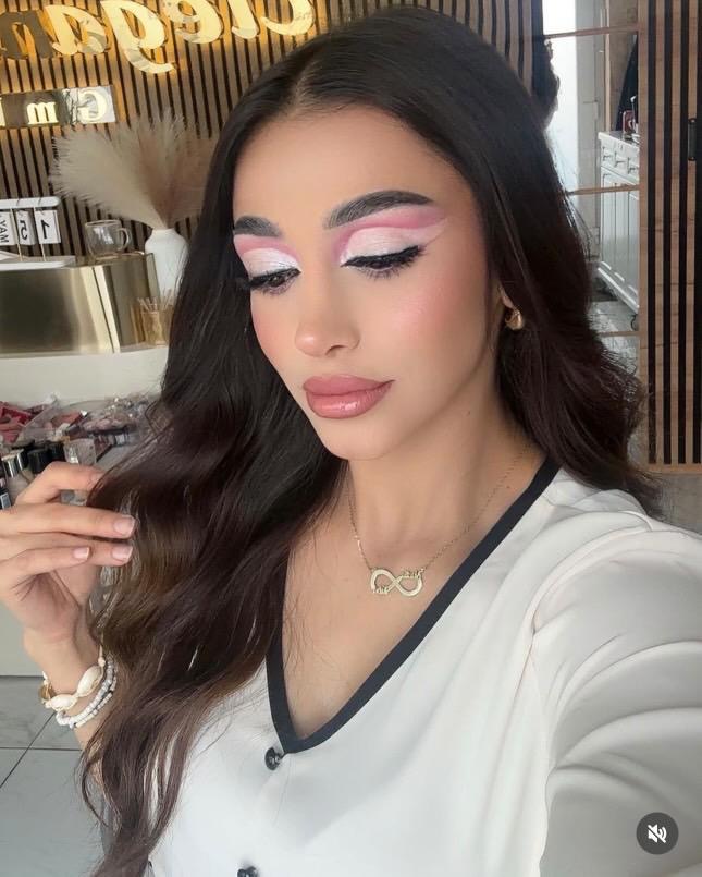 Eine Frau mit langem, dunkelbraunem Haar und auffälligem rosa Augen-Make-up.
