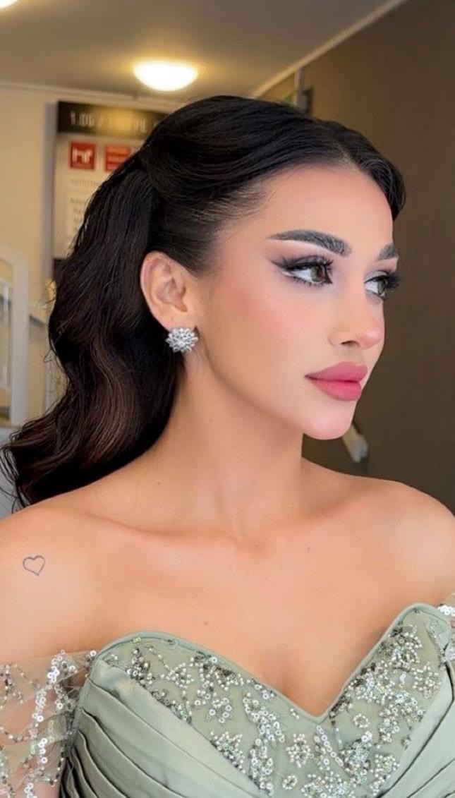 Eine Frau mit elegantem Make-up und langen dunklen Haaren trägt ein verziertes, hellgrünes Kleid.